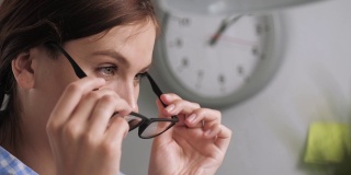 女孩戴上了眼镜。特写的年轻女性在工作场所在办公室或公寓谁戴上眼镜的视力或在电脑上工作