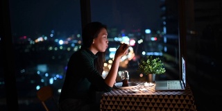一个亚洲的中国美丽的年轻女士在她的公寓里吃甜点在神奇的时间，黄昏和她的男朋友通过互联网聊天用她的笔记本电脑
