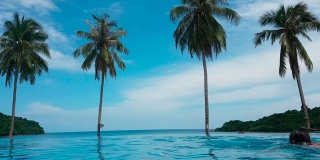 亚洲女人放松在暑假假期无限游泳池与蓝色的大海在阳光灿烂的一天。健康幸福的生活方式和看海滩的景色。