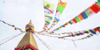 在尼泊尔加德满都的博达佛塔(Boudhanath)上，以蓝天为背景的4K多色佛教旗帜和咒语在狂风中飘扬的画面。