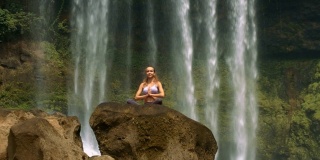坐着的女人在水墙旁边的岩石上冥想瑜伽