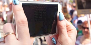 女孩的手在智能手机上取下的特写一大群人走在街上，慢镜头