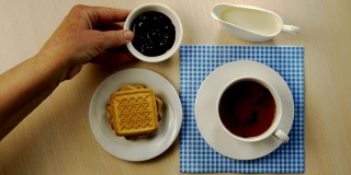 一杯茶，一碟饼干，一碗果酱和牛奶壶放在明亮的桌子上。