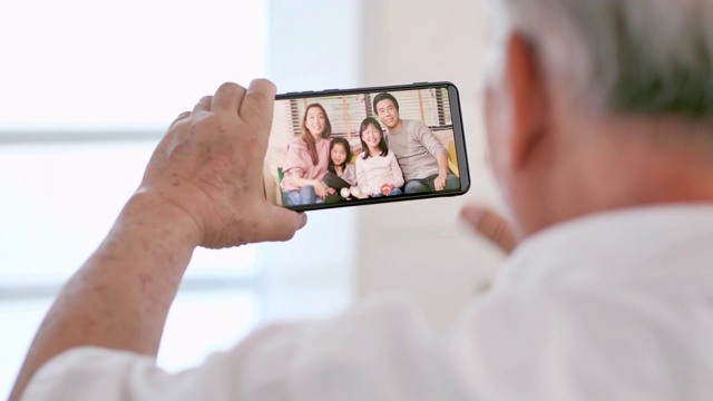 亚洲老爷爷在视频会议上与在国外的女儿家人进行视频通话，在社交过程中使用智能手机和视频会议技术保持距离。社会电话会议