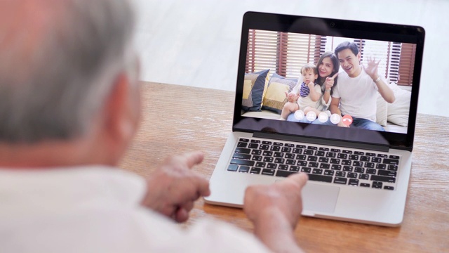 亚洲老爷爷在视频会议上与在国外的女儿家人进行视频通话，在社交过程中使用电脑和视频会议技术保持距离。社会电话会议