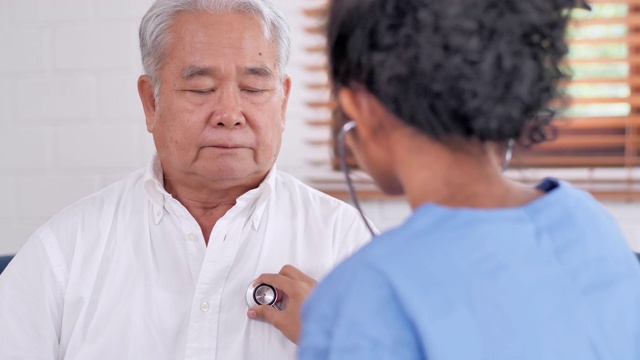 年轻黑人女护士医生为亚洲老年男性检查心脏，以预防冠状病毒或Covid-19在家里流行。采购产品医疗，护理，护理，退休，志愿者，慈善，教育，养老院，在家照顾者，医药和卫生保健