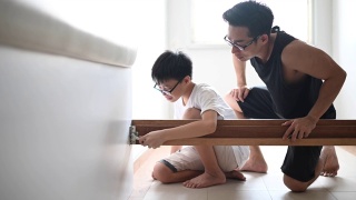 一个亚裔华人家庭搬家父子组装床架视频素材模板下载