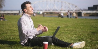 男孩正在检查笔记本电脑，收到了好消息。一个男人坐在公园里，男人刚刚赢得了一个巨大的奖，终于发生了。一个学生，一个自由职业者，微笑着，大笑着。胡椒咖啡。