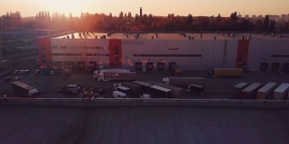 在美丽的夕阳下，飞过物流中心仓库的屋顶，飞过装载货物的卡车