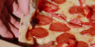 一片辣香肠披萨。人的手从打开的盒子里拿起一片片热辣美味的意大利披萨，送餐