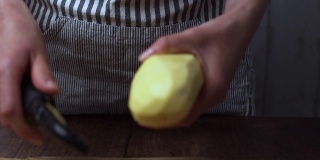 一个女人用菜刀削大土豆的手的特写。准备土豆的概念。