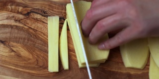 把大土豆切成楔形，准备炸薯条。在木板上切土豆。一个女人的手切土豆。