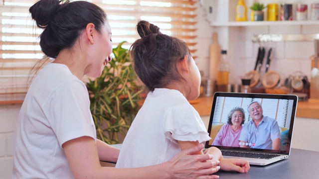 亚洲母亲和女儿在视频会议上与国外的祖父母家庭视频电话，在社会距离使用笔记本电脑和视频会议技术。社会电话会议