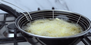 在煤气炉上的平底锅里的一个篮子里，自制的炸薯条在沸腾的油里冒着很多泡泡。炸薯条因为他们的烹饪而成为黄金。