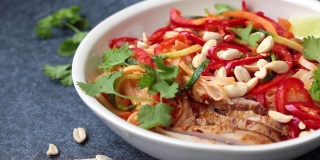 吃泰式炒面与鸡肉，花生和蔬菜在碗，深色背景。