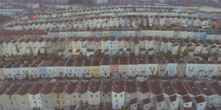 向前飞行的航拍，倾斜到水平排列的彩色梯级英国房屋，以布里斯托尔中部为背景
