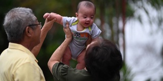 一对亚洲华人老夫妇和他们的孙子在自家前院玩