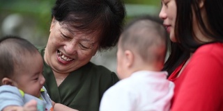 一位年长的亚洲华人妇女和她的双胞胎儿子孙子在他们家的前院和她的女儿一起玩
