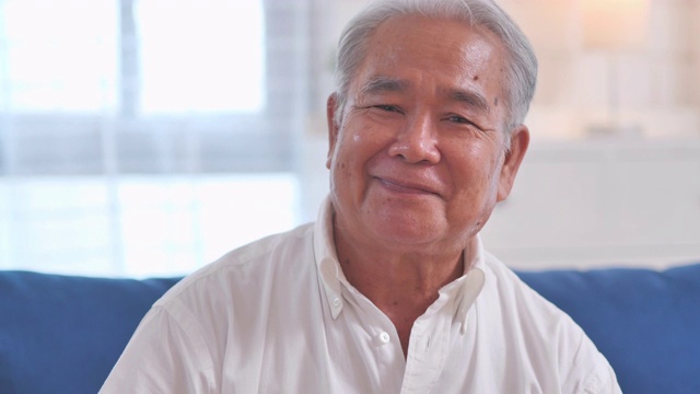 肖像自信的亚洲老爷爷微笑着与镜头交流，独自在家摆姿势，快乐的情绪享受成功的生活方式。在视频会议技术上的社交距离。家庭工作室