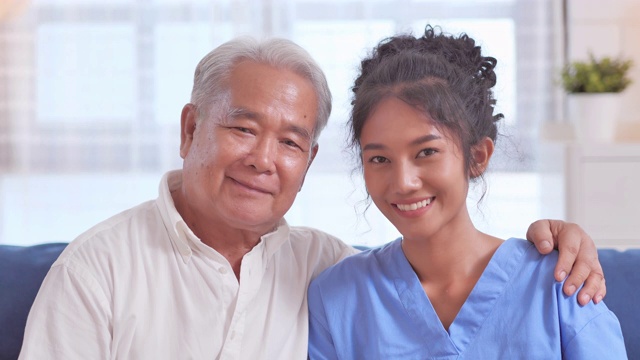 肖像快乐的志愿者年轻的黑人妇女护士看门人与亚洲老祖父病人，同时看在家里的相机。家庭工作室