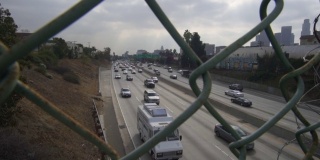 在多云的日子里，通过慢动作的链链围栏在洛杉矶繁忙的高速公路交通的观点