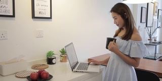 一名亚裔中国妇女在家喝咖啡时用笔记本电脑工作