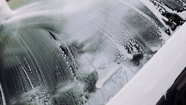 男人的手用海绵和泡沫擦洗汽车的挡风玻璃。汽车服务理念，