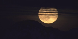 一轮超级满月透过云层越过山脉