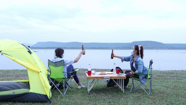 两个亚洲女人在湖边露营的时候一起喝着啤酒