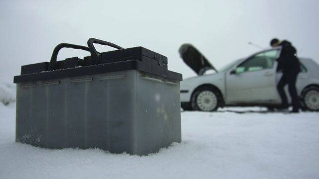 在冬天下雪的时候，有人修理坏了的汽车。汽车故障或问题。汽车电池躺在汽车旁边。引擎盖或引擎盖抬起。典型的铅酸蓄电池具有重要的应用前景