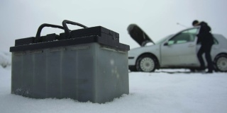 在冬天下雪的时候，有人修理坏了的汽车。汽车故障或问题。汽车电池躺在汽车旁边。引擎盖或引擎盖抬起。典型的铅酸蓄电池具有重要的应用前景