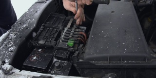 修理或修理后，工人将充电的汽车电池安装在车内。汽车故障或问题。在冬季白天停车时，引擎盖或引擎盖抬高。铅酸电池的特写。Slowmo