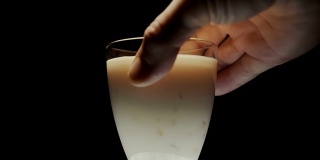 一名男子从一个白色塑料瓶中，将牛奶酸奶和水果倒入玻璃杯中