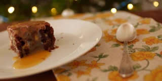 一块方形的巧克力布朗尼蛋糕放在一个盘子里，在一个木制的背景上，一张有黄色花朵的餐巾和一个旧的梅尔基奥勺子。金黄的咸味焦糖慢慢沥干。