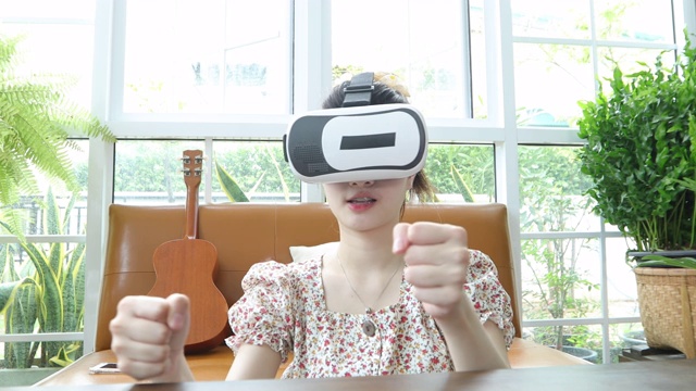 亚洲女性使用平板电脑和虚拟现实模拟器在客厅玩游戏，感到快乐。居家养老理念