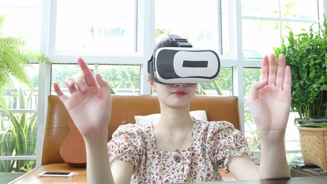 亚洲女性使用平板电脑和虚拟现实模拟器在客厅玩游戏，感到快乐。居家养老理念
