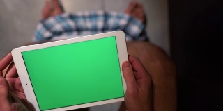 男人坐在厕所的壶上。手持平板电脑，放大和滑动。绿色的屏幕。独自在厕所里。裤子躺在脚上。腹泻