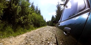 绿色汽车行驶在破旧的石头路在农村地区的木材。夏天的时间