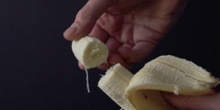 在一个黑暗的特写背景上，一个男人的手掰下了一根成熟的香蕉