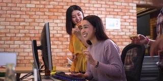 低角度视角:亚洲年轻漂亮的女商人穿着休闲的衣服参加聚会，面带微笑，在现代的办公室里用电脑工作到很晚，与同事一起享受快乐。积极的工作幸福感的概念。
