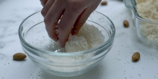 将白巧克力碗浸入/混合在玻璃碗里的干椰子中。准备自制椰子巧克力的概念。