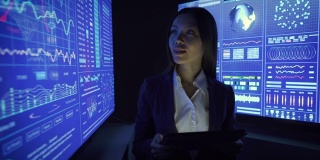 在黑暗的实验室里用平板电脑和显示器工作的女商人