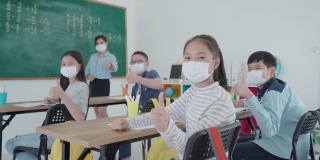 一群亚洲小学生和教师戴着卫生口罩在教室里防止Covid - 19的爆发，返校时重新开学，教育理念的新常态。