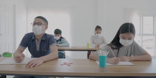 一群亚洲小学生戴上卫生口罩在教室里防止Covid - 19的爆发，返校时重新开学，教育理念的新常态。