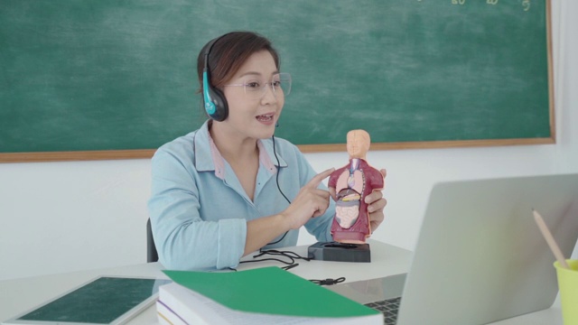 亚洲女教师通过视频会议和课堂上的黑板在笔记本电脑上学习生理科学。在家教育和远程学习，在线，教育和互联网。