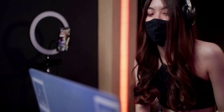 戴着黑色面具的亚洲女性dj在笔记本电脑和转盘上播放音乐，戴着面具的亚洲女性在俱乐部调音隔离新冠病毒，在线直播演出，在线自由职业者工作