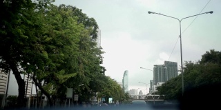 乘客座位上的视野望向汽车前挡风玻璃，街道一侧的树木，亚洲城市道路，紫外线防护，热车窗玻璃，开始旅程，城市建筑天空景观在中心