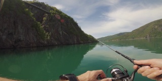一名男子在挪威峡湾边的一艘小船上用鱼竿钓鱼