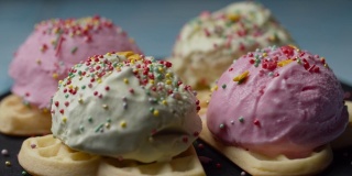 自制华夫饼与彩色冰淇淋顶部旋转。在慢镜头中，糕点顶部落在华夫饼上的粉色和绿色的冰淇淋球上。