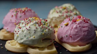 自制华夫饼与彩色冰淇淋顶部旋转。在慢镜头中，糕点顶部落在华夫饼上的粉色和绿色的冰淇淋球上。视频素材模板下载